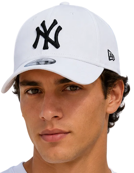 A close-up of a man wearing a white New York Yankees baseball cap with a black embroidered NY logo on the front and a black New Era flag logo on the side, set against a light blue sky background.