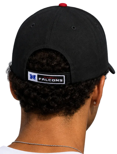 shown from behind wearing black baseball caps with a white and blue Falcons logo patch on the back, set against a clear blue sky.