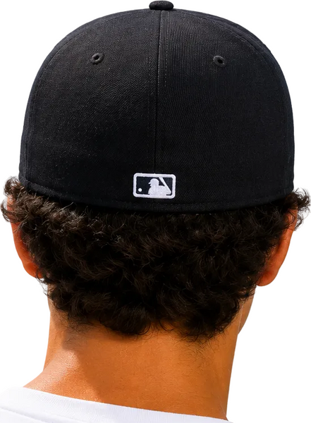 Two people seen from behind wearing black baseball caps with a small white MLB logo on the back, set against a clear blue sky.